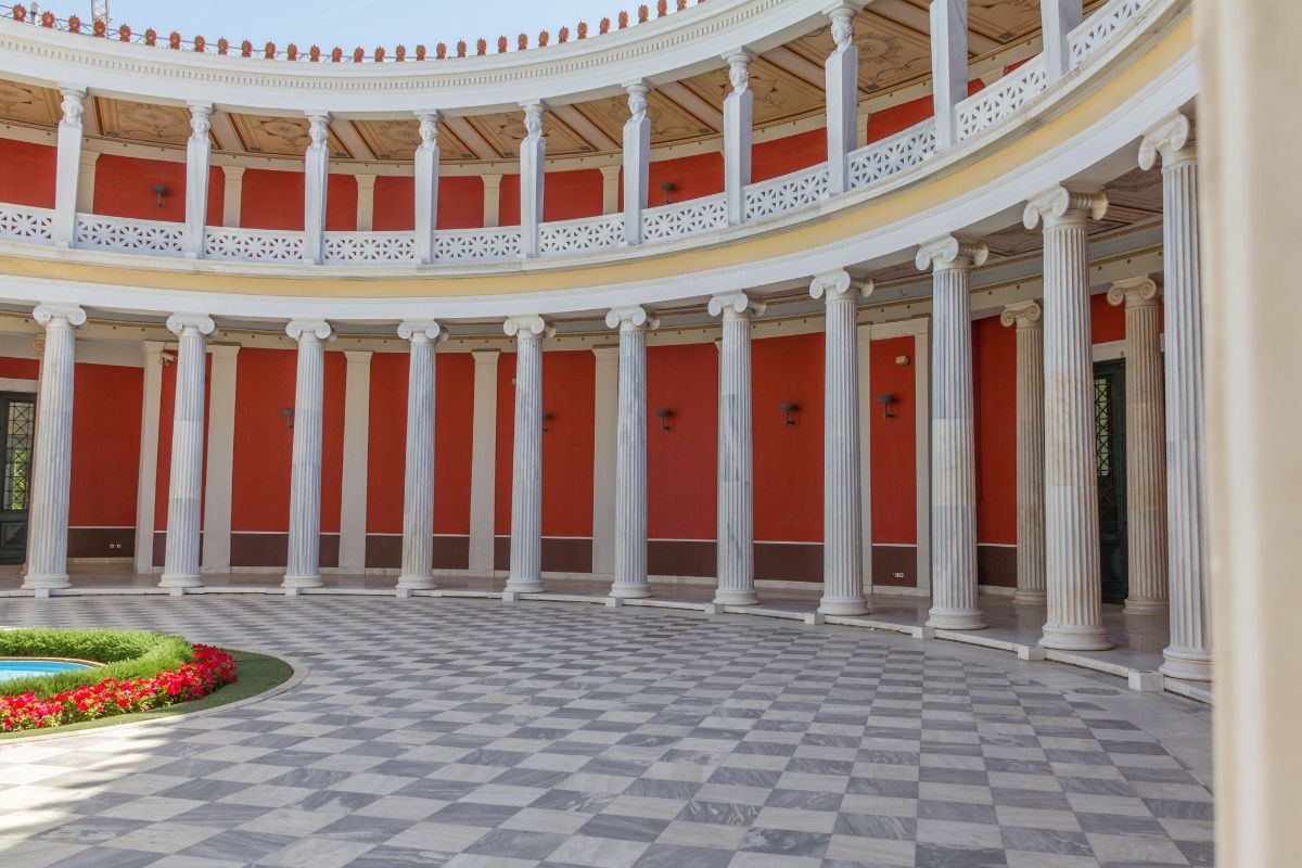 A circular neoclassical courtyard with a checkered floor, surrounded by columns and red walls, with a section of balustrade visible above.
